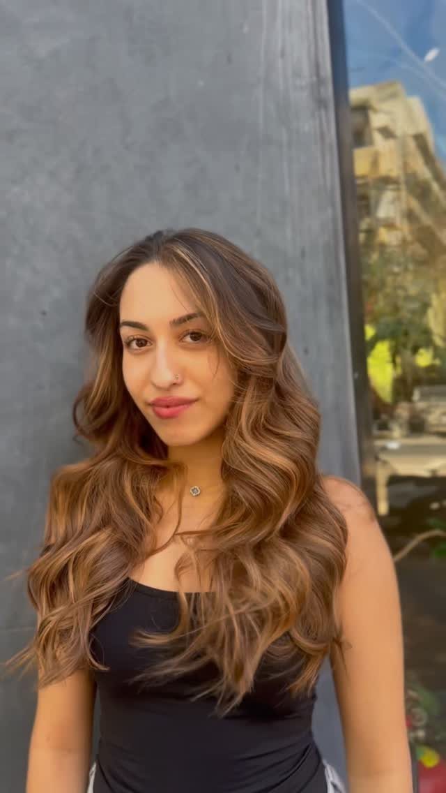 16 Dark Brunette Hair Color Ideas for Every Skin Tone 11 Woman with long wavy golden brown hair and highlights posing by a wall