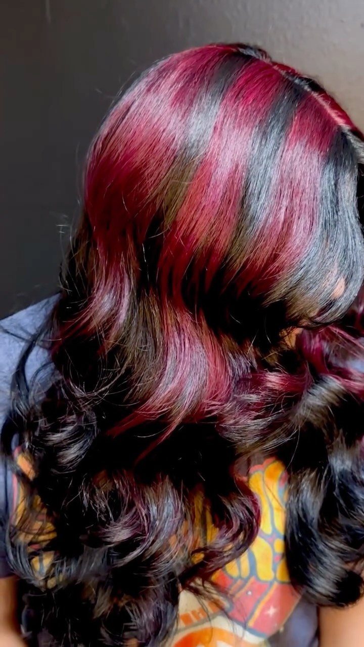 Long wavy dark hair with vibrant raspberry and burgundy highlights in curls.