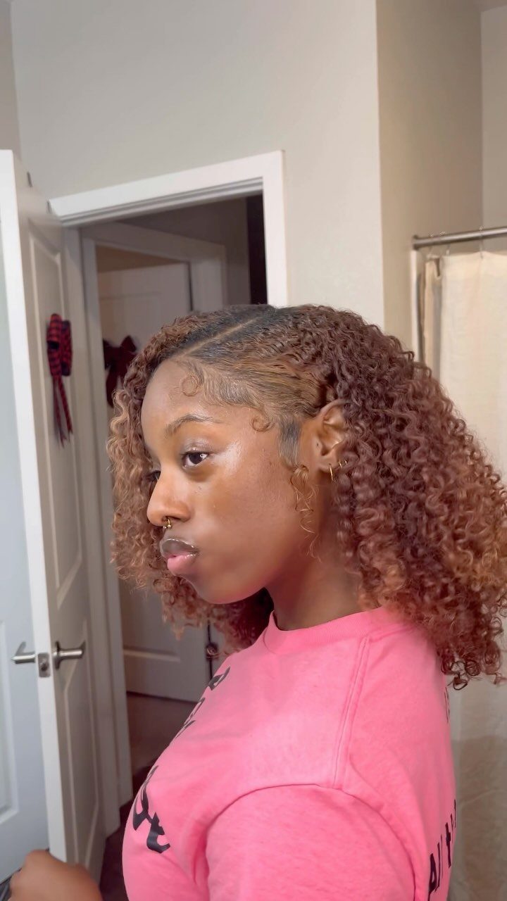 16 Easy Hair Styles for Beginners to Try at Home 6 Woman with honey-brown curly hair wearing a pink t-shirt in a bathroom setting.