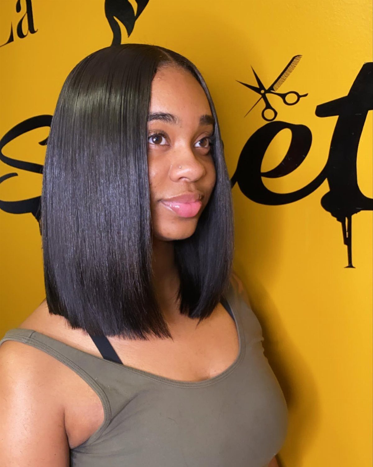 18 Easy Hairstyles for Medium Hair You Can Do Fast 6 Woman with a sleek black middle part bob haircut against a yellow wall.