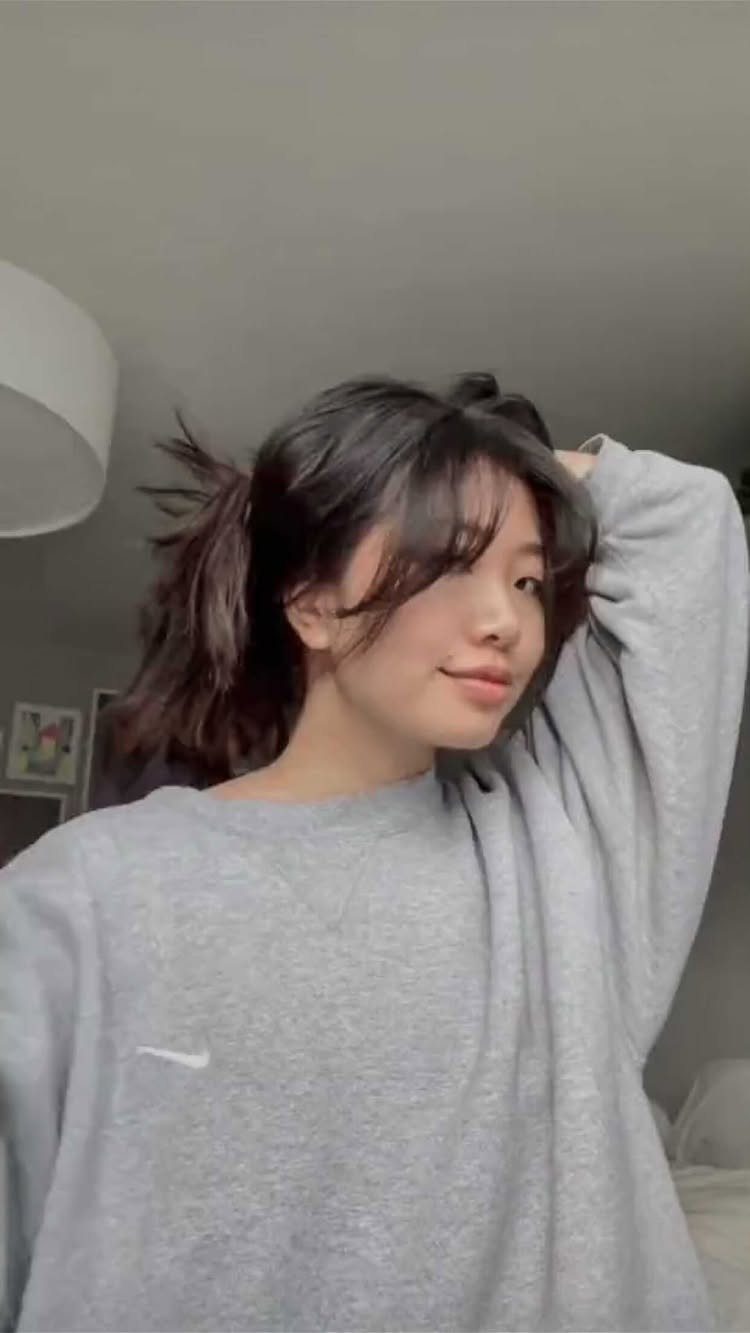 Fall Hair Dos with 15 Ideas from Burnt Copper to Claw Clips 2 Young woman with dark hair and wispy face framing bangs wearing grey sweatshirt.
