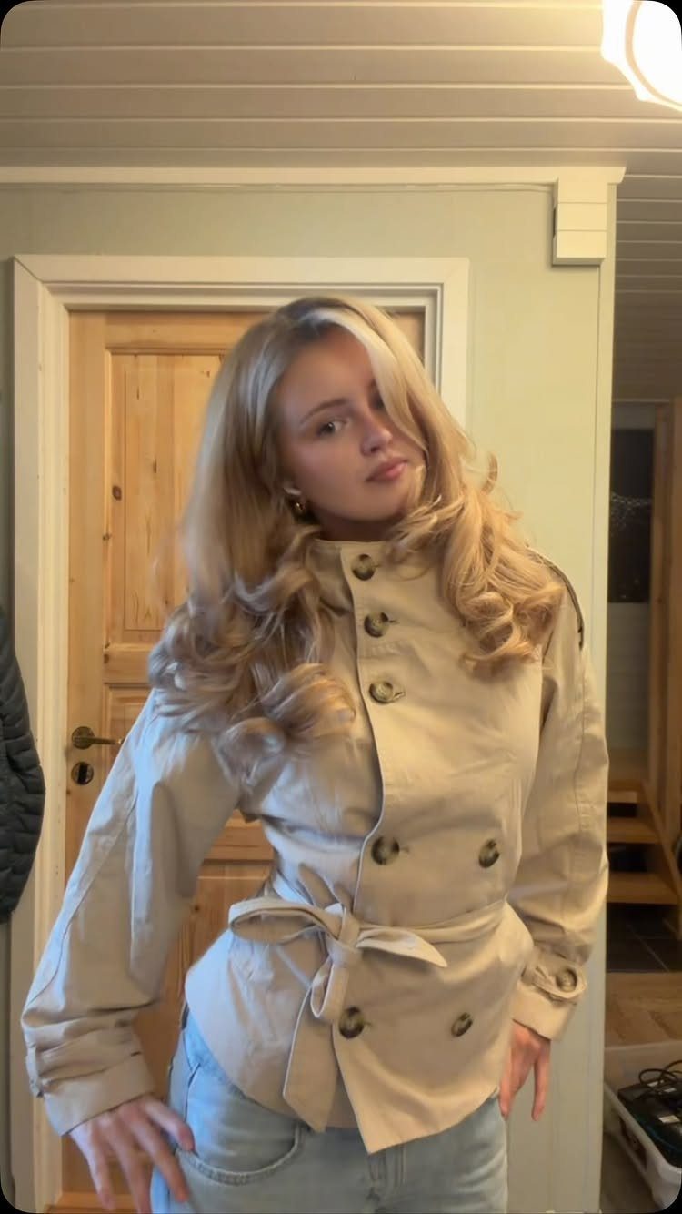 Fall Hair Dos with 15 Ideas from Burnt Copper to Claw Clips 8 Woman with voluminous blonde hair in a soft blowout wearing a beige trench coat.