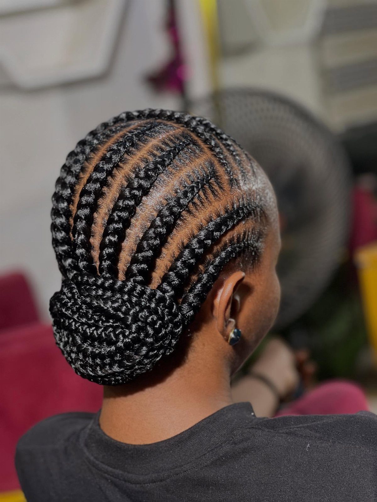 Woman with black cornrows styled into a braided bun at the nape.