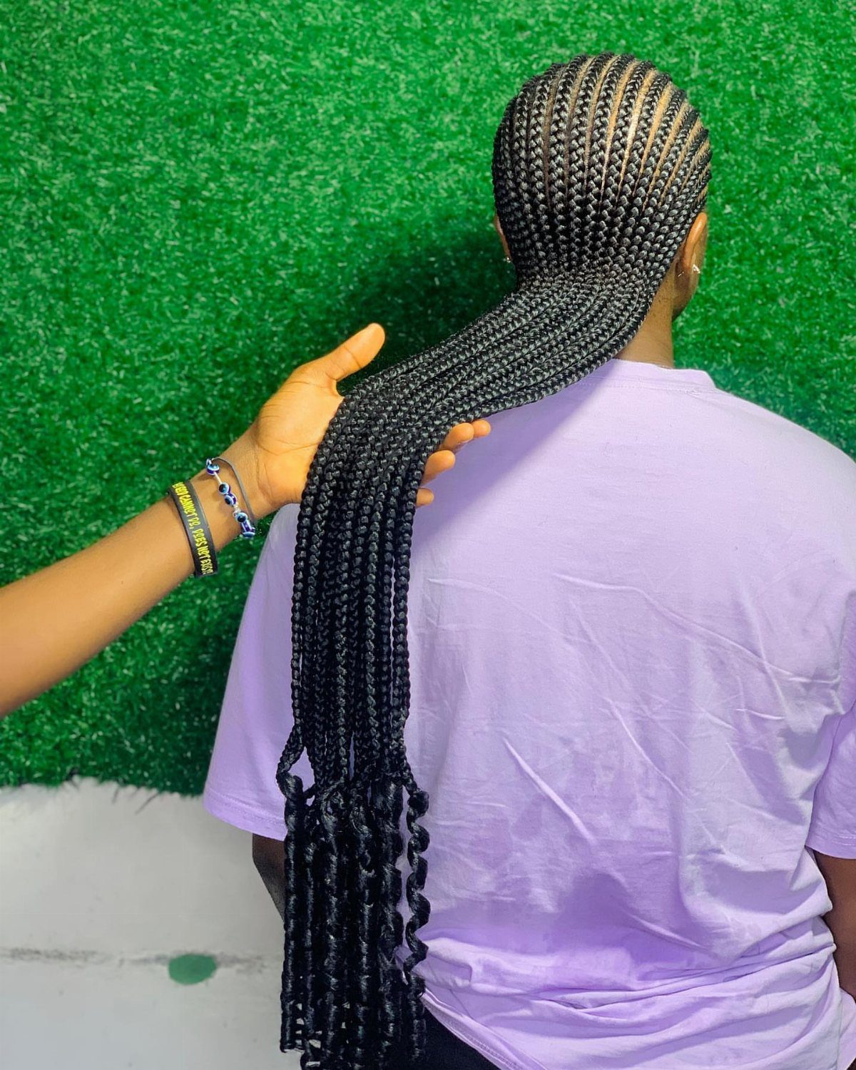Long black straight-back cornrow braids on a person wearing a purple shirt.