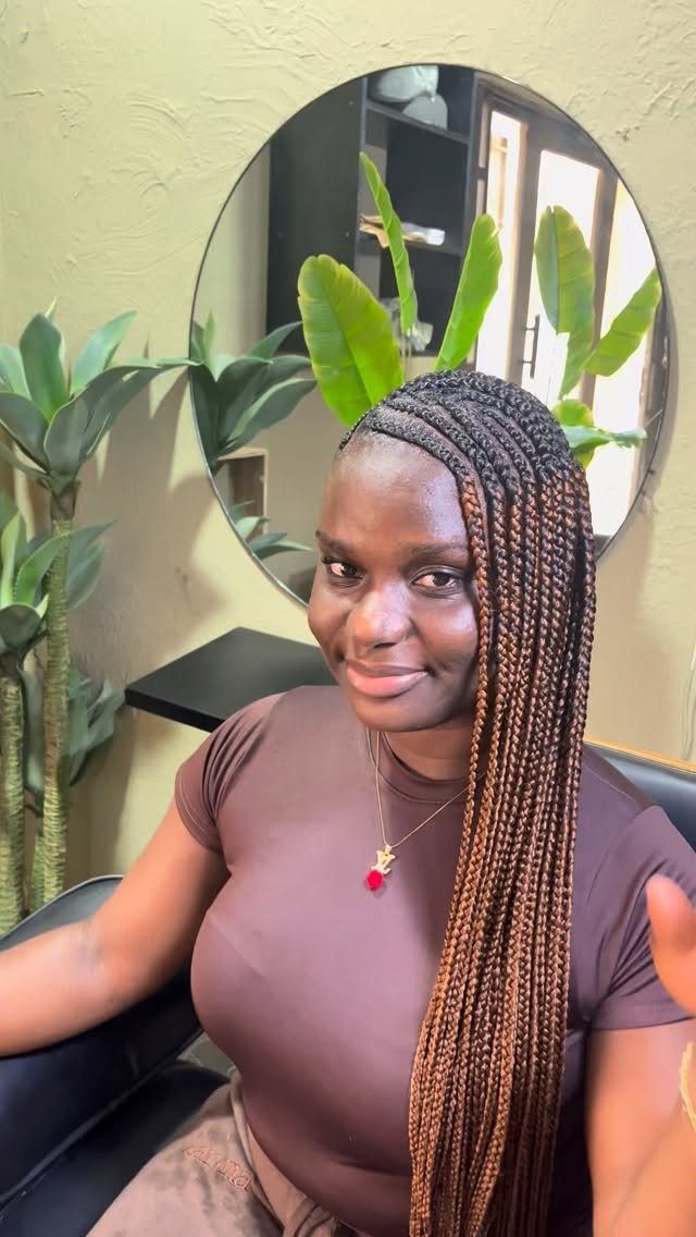 Woman with long brown box braids swept over one shoulder in a room.