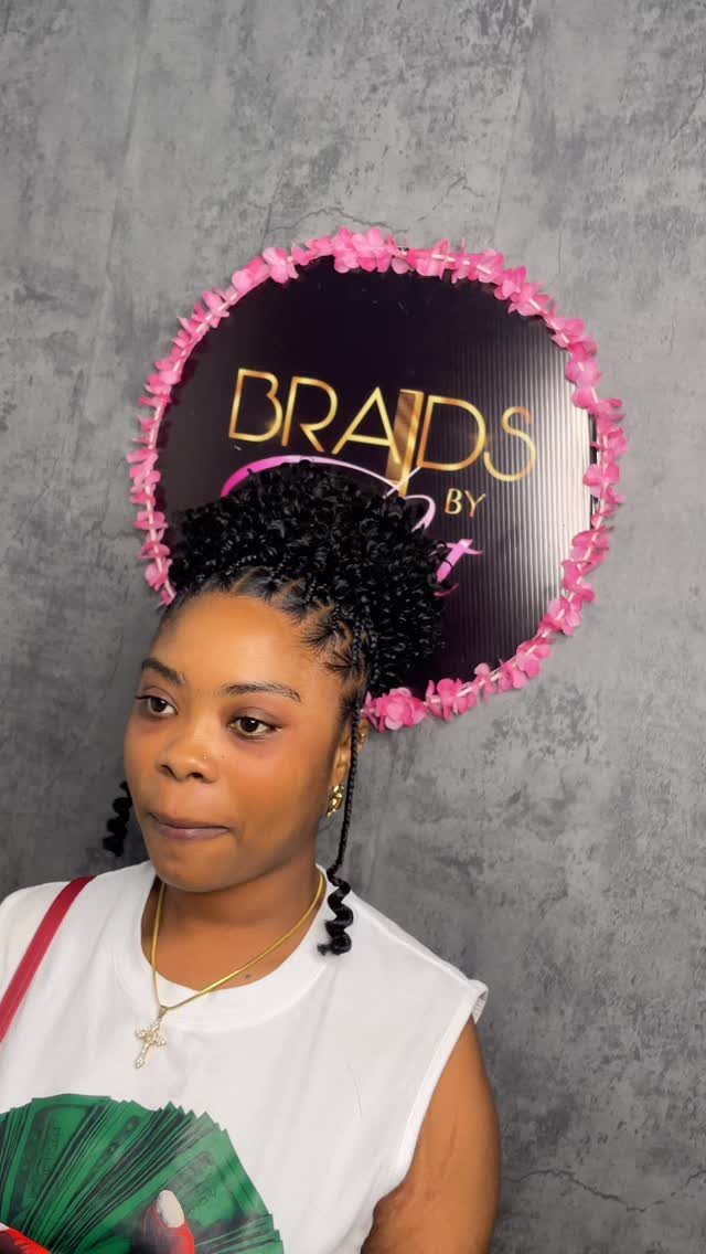 12 Good Hairstyles for Curly Hair, From Bangs to Braids 10 Woman with a high curly updo hairstyle posing in front of a floral sign.
