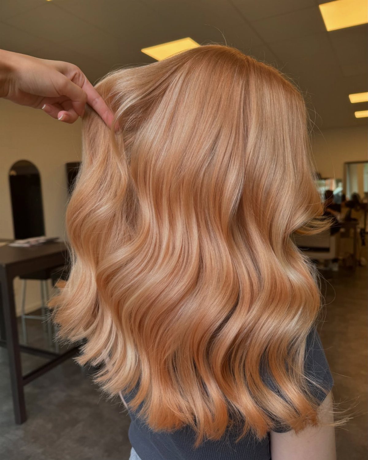 22 Hair Color Red and Blonde Ideas for Every Length 20 Wavy copper hair with strawberry blonde highlights in a bright hair salon setting.