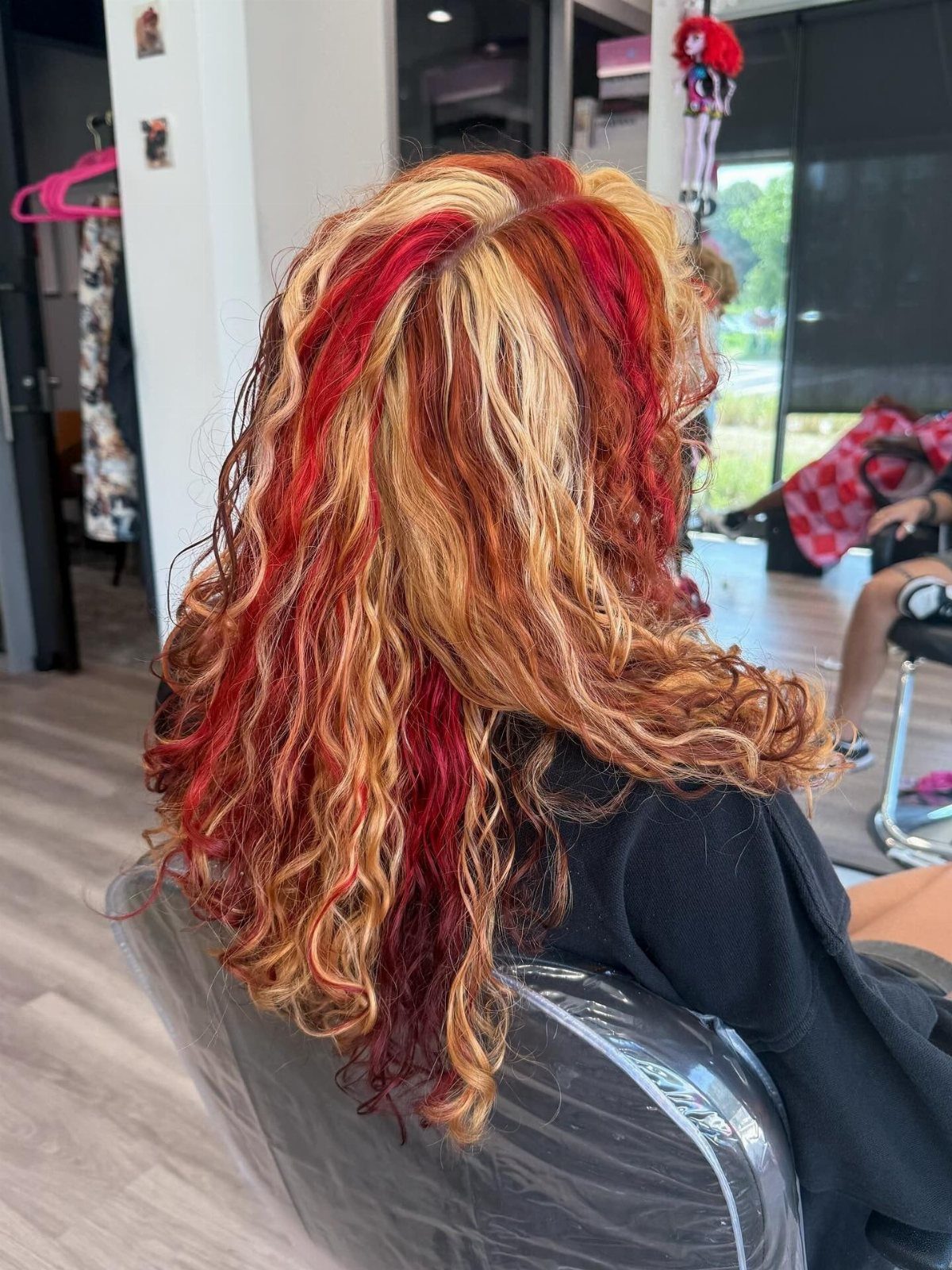 22 Hair Color Red and Blonde Ideas for Every Length 12 Long curly hair with vibrant red and golden blonde highlights in a salon.