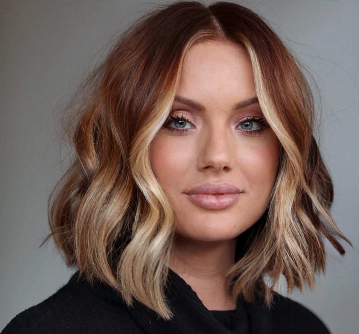 22 Hair Color Red and Blonde Ideas for Every Length 3 Woman with a wavy red layered bob and light blonde face-framing highlights.