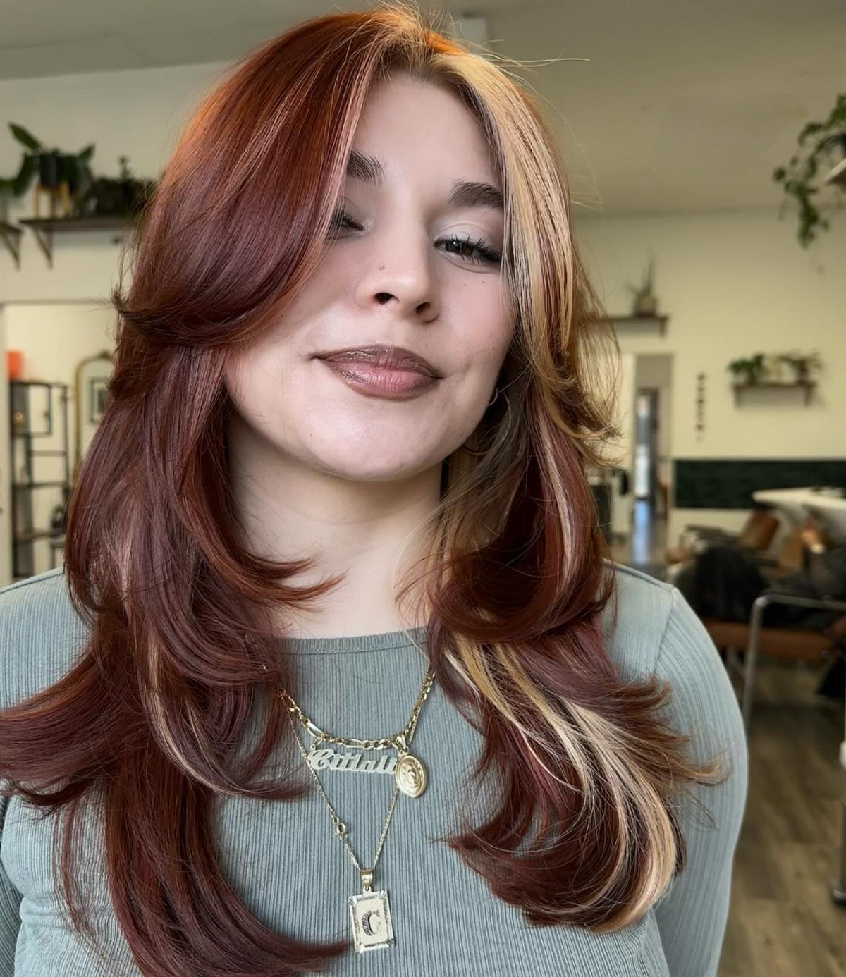 22 Hair Color Red and Blonde Ideas for Every Length 1 Woman with long wavy red hair and blonde highlights wearing gold necklaces.
