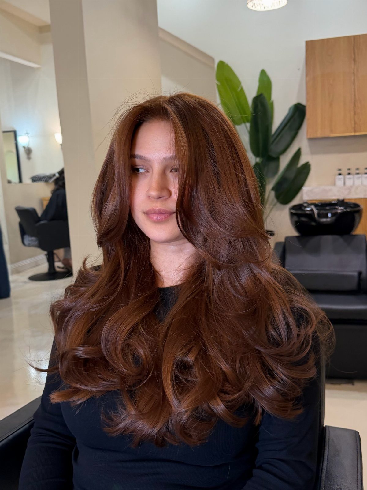Hair Colour Ideas Brown: 13 Shades From Chestnut to Mahogany 9 Woman with long, wavy burnt sienna reddish-brown hair posing in a hair salon.
