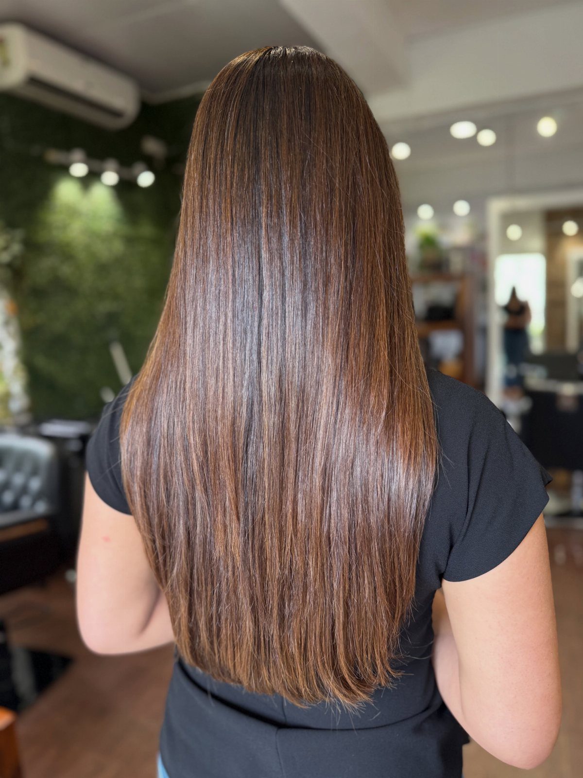 Hair Colour Ideas Brown: 13 Shades From Chestnut to Mahogany 4 Long straight brown hair with golden highlights seen from the back in a salon.