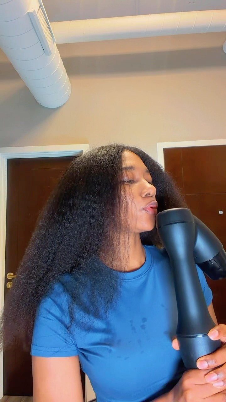 3 Hair Dryers for Natural Hair: Handheld, Diffuser, Brush 1 Woman with voluminous natural hair using a black hair dryer in a room.