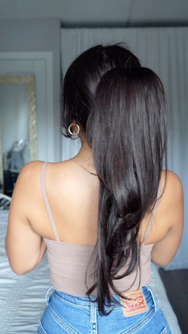 Woman with long, smooth dark brown hair seen from behind wearing blue jeans.