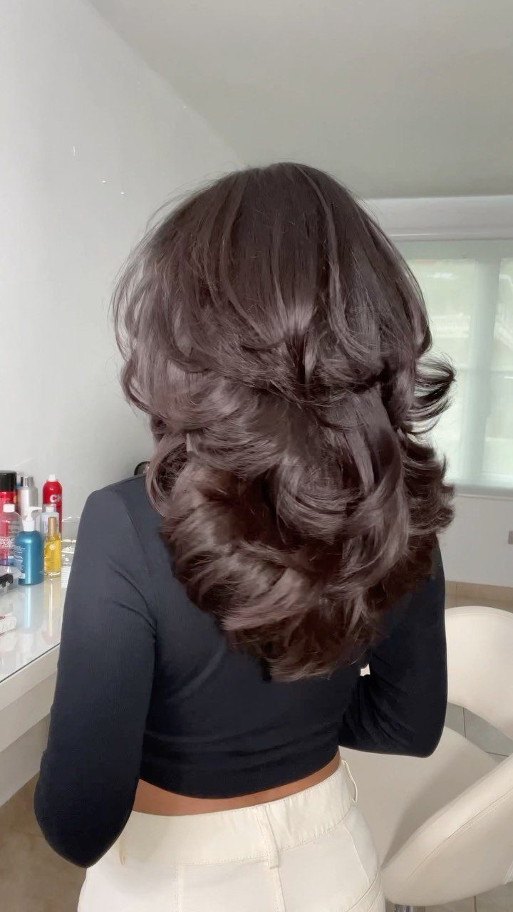 Woman with voluminous, layered dark brown hair styled in large curls from behind
