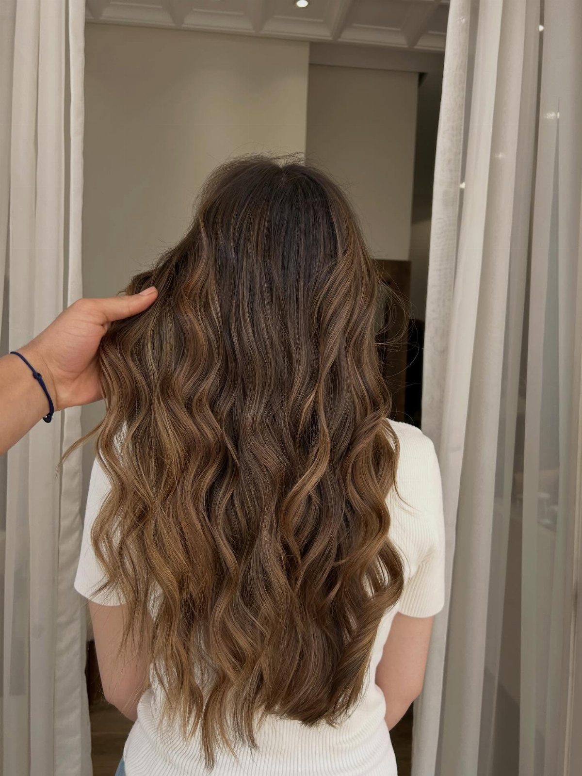 Long brown wavy hair with highlights seen from behind in a bright room