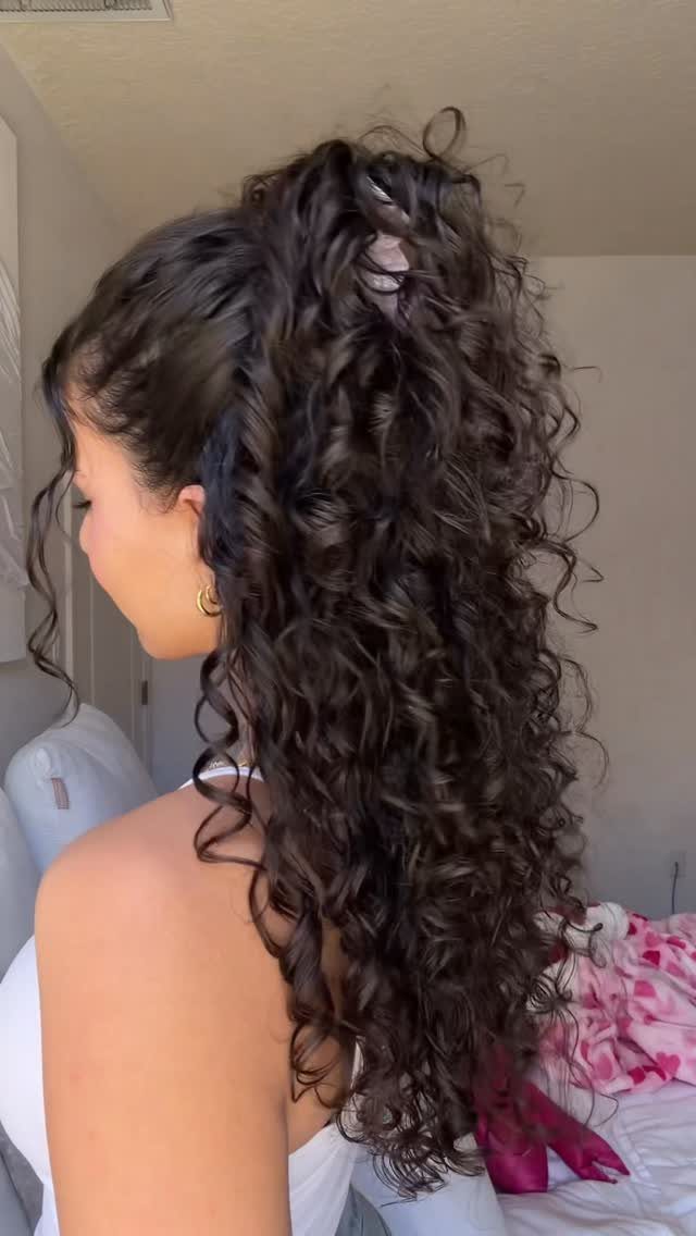 Woman with long dark curly hair styled in a half-up ponytail from side view