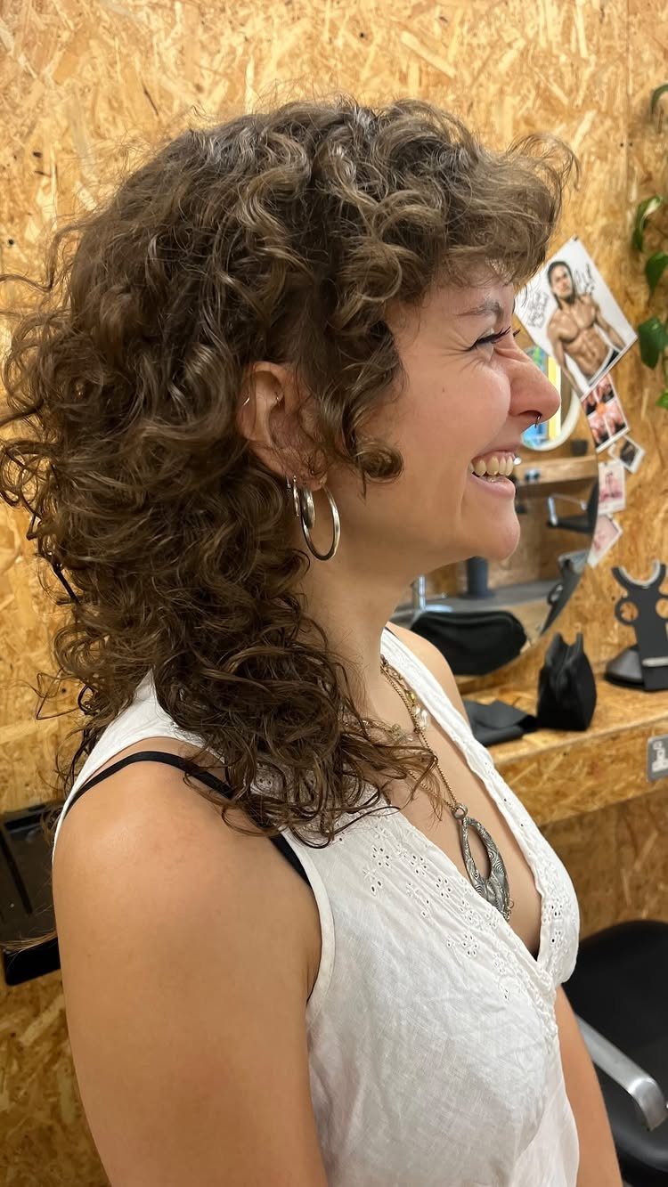 Woman with a curly brown shag haircut smiling in a profile view.