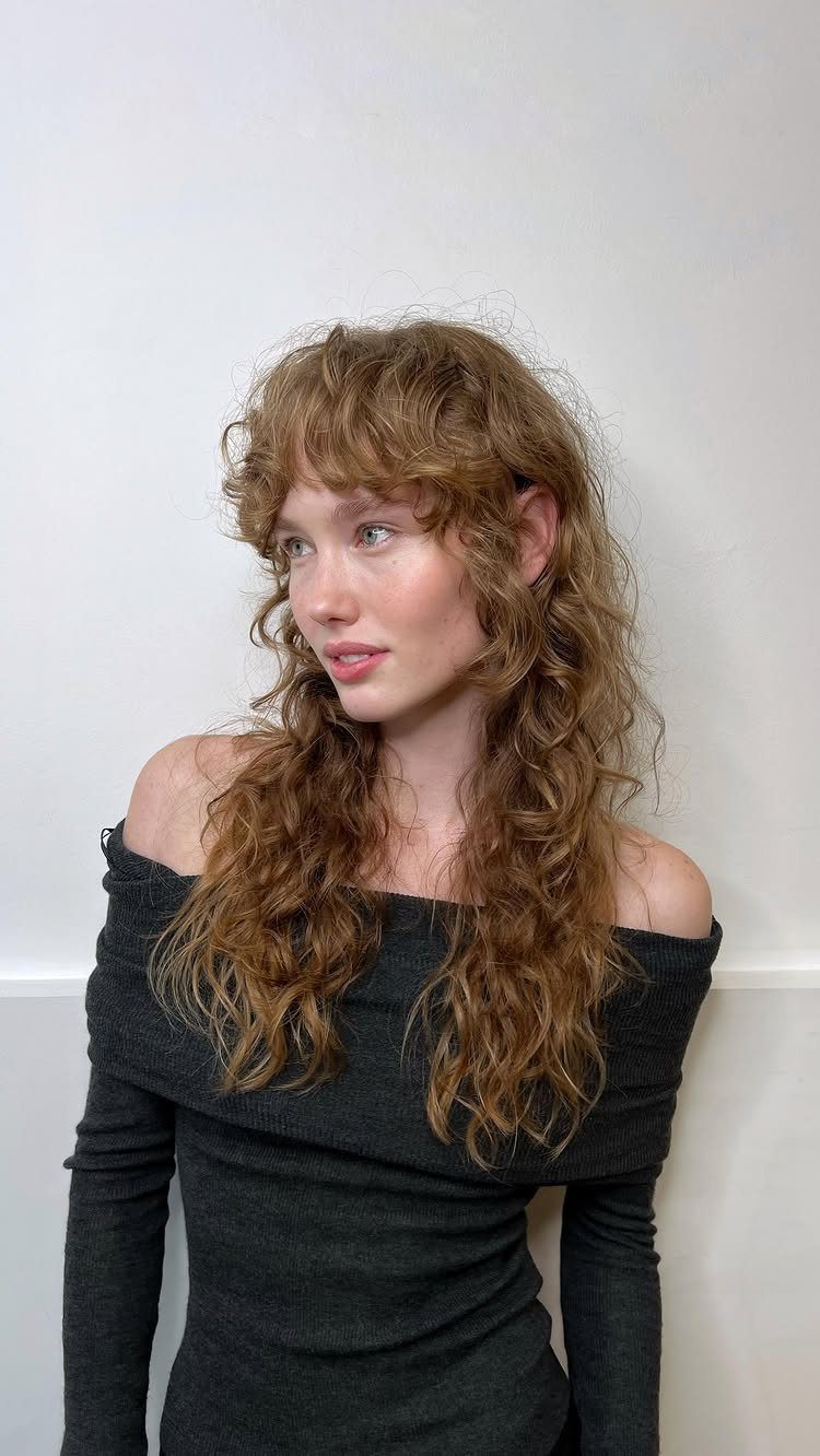 Woman with long curly reddish-brown hair featuring soft curtain bangs and layers.