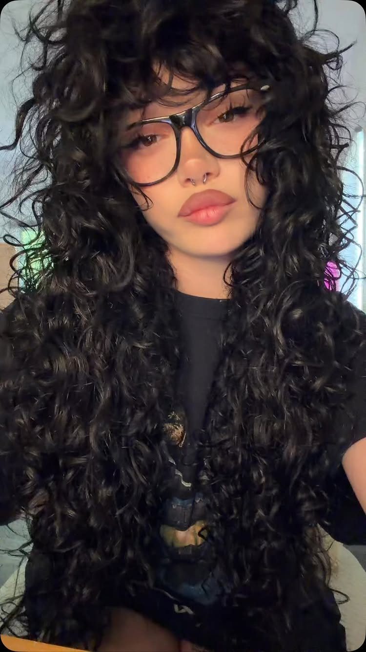 Person with long voluminous curly dark hair and bangs wearing black glasses
