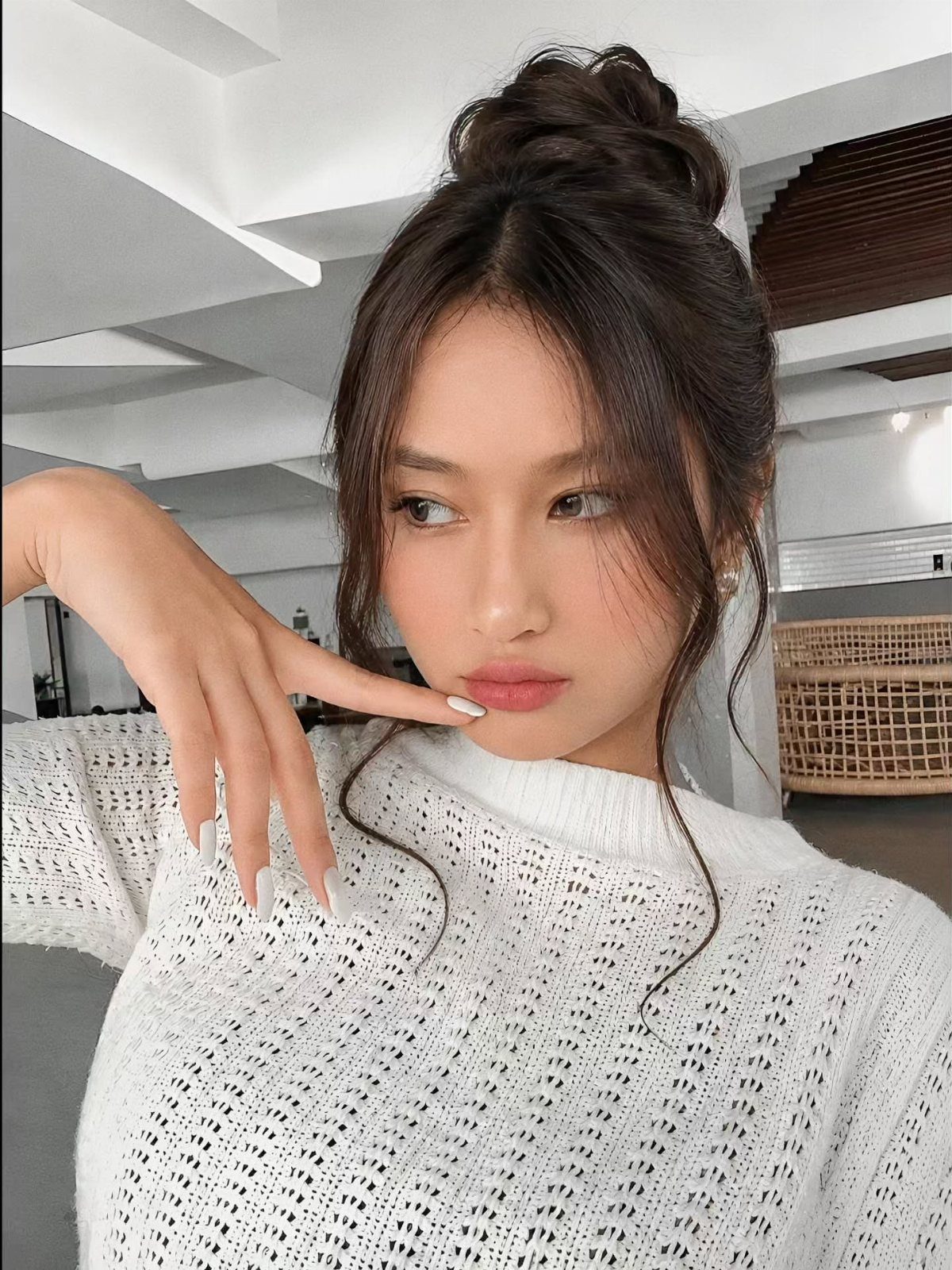 15 Ways to Pick a Hairstyle for Sweater Weather 2 Woman with a high bun hairstyle wearing a white knitted sweater posing indoors.