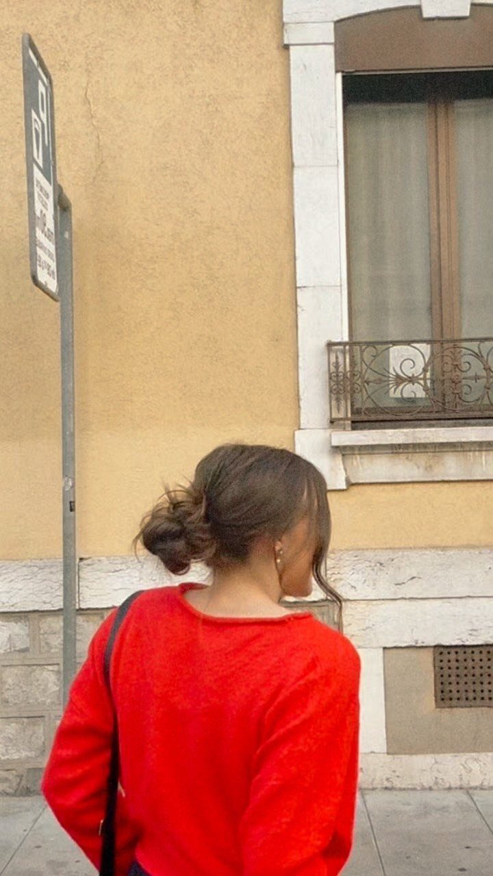 15 Ways to Pick a Hairstyle for Sweater Weather 14 Woman in red sweater with brown hair styled in a low messy bun.