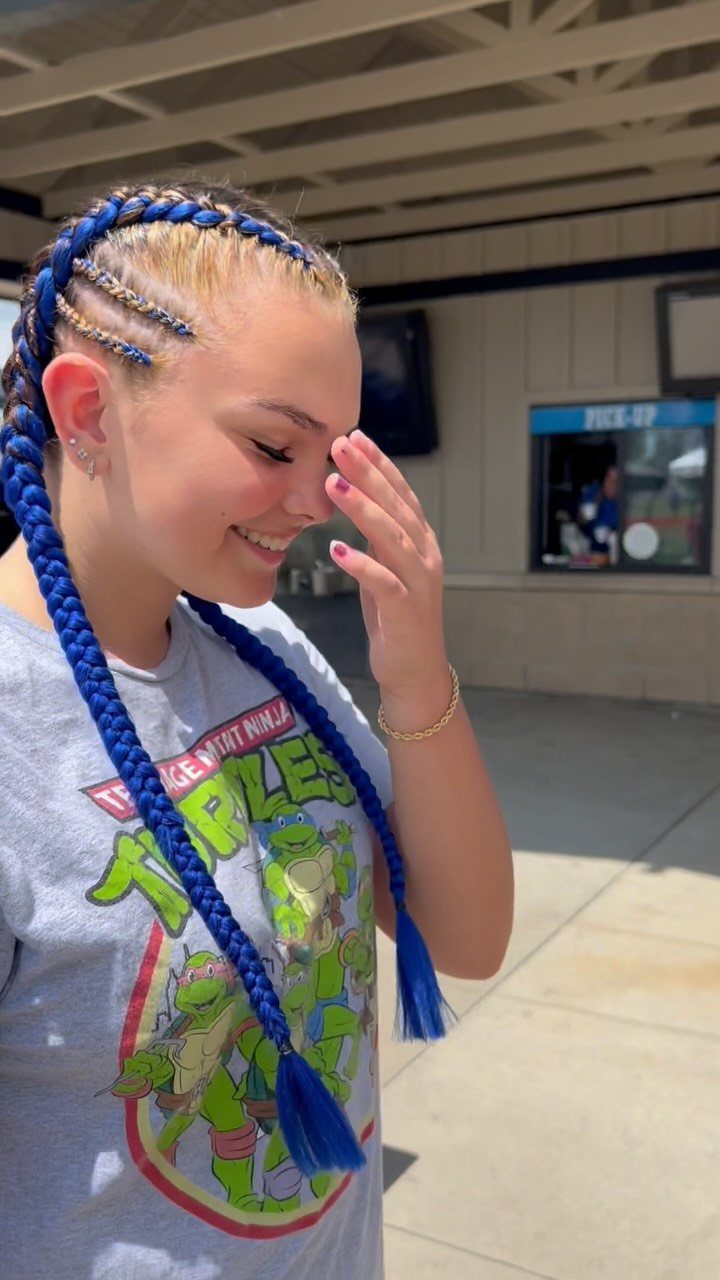 17 Hairstyles for Football Games: Braids, Buns & Ponytails 17 Young woman with blonde and blue braided hair wearing a graphic t-shirt.