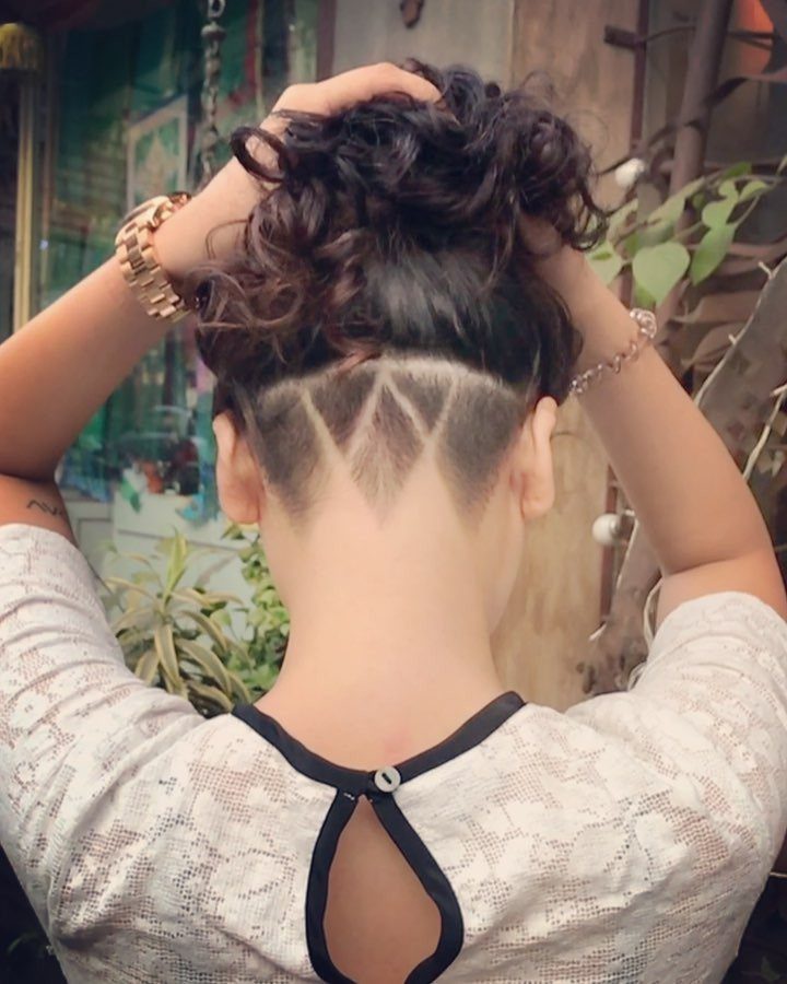 Person with curly hair in a bun and a geometric shaved undercut design