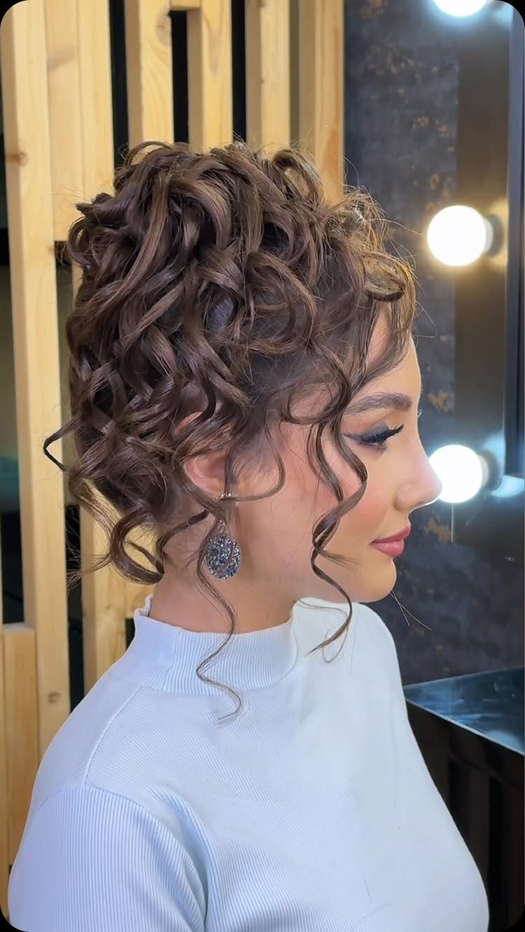 Woman with a curly updo and loose face-framing tendrils in a studio setting.