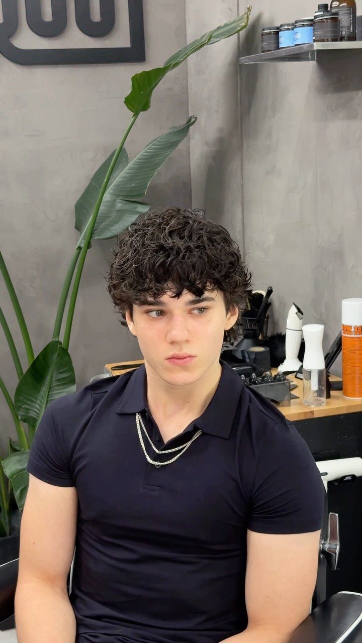 Young man with dark curly hair and a textured wavy fringe in a barbershop.