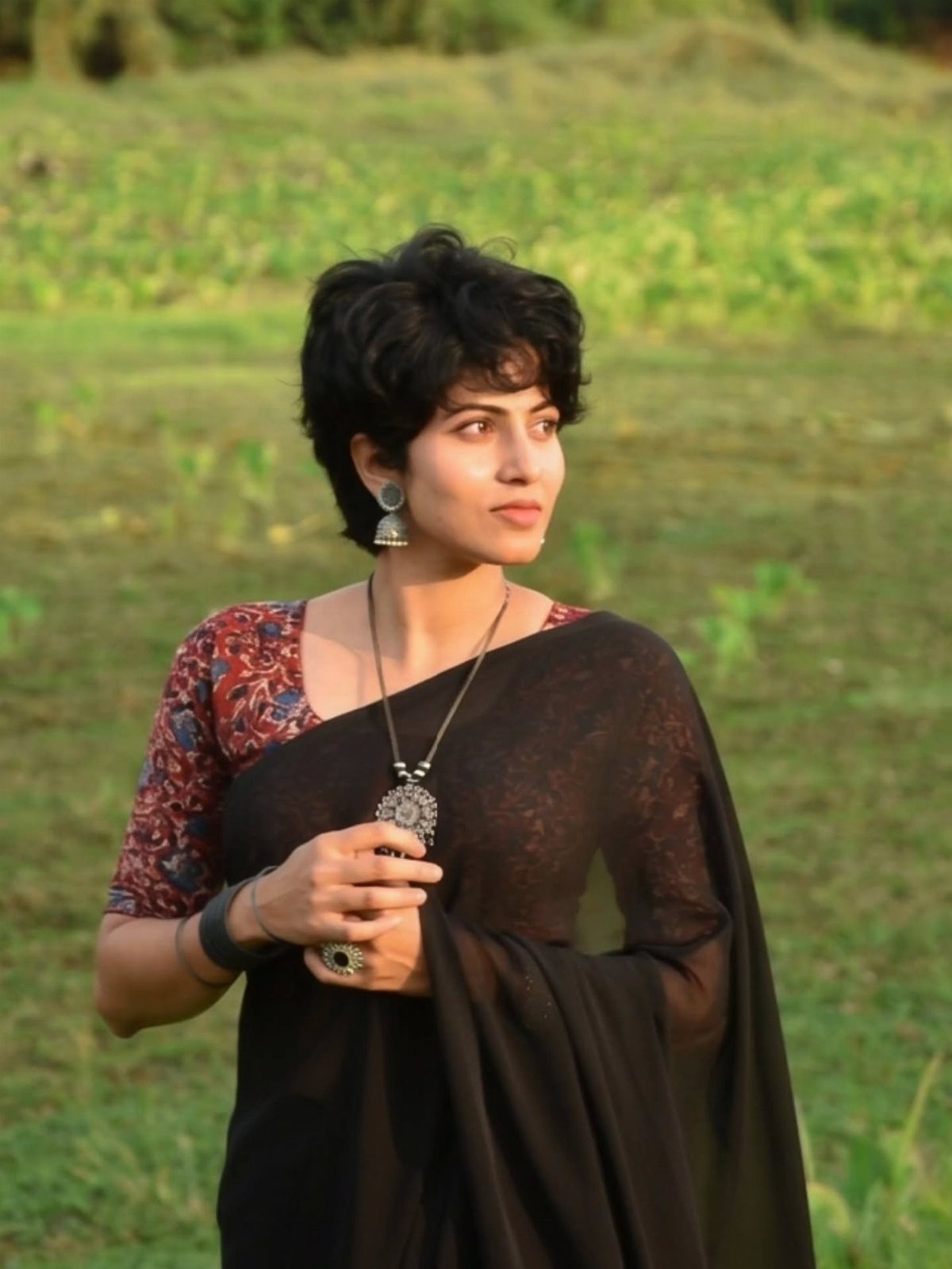 10 Hairstyles on Saree for Every Look and Occasion 8 Woman with short wavy black hair wearing a black saree in a field
