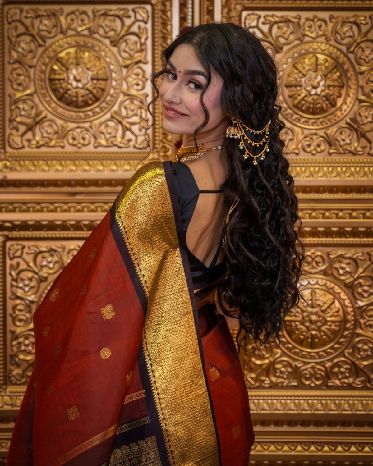 10 Hairstyles on Saree for Every Look and Occasion 2 Woman in red saree with long side-swept curls and gold jewelry