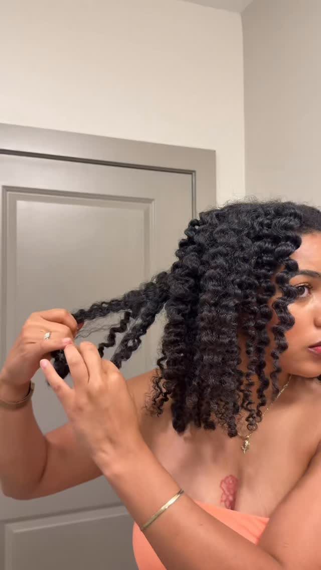 22 Hairstyles for Real Hair, from Bantu Knots to Bobs 7 Woman with defined curly hair touching a curl in a home setting.