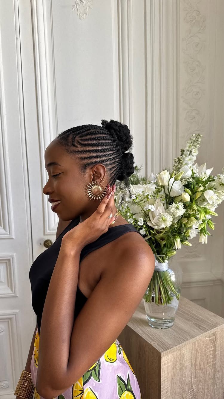 22 Hairstyles for Real Hair, from Bantu Knots to Bobs 5 Woman with braided hair in a bun posing next to white flowers.