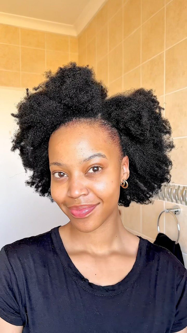 22 Hairstyles for Real Hair, from Bantu Knots to Bobs 9 Woman with voluminous natural hair styled into two large curly puffs.