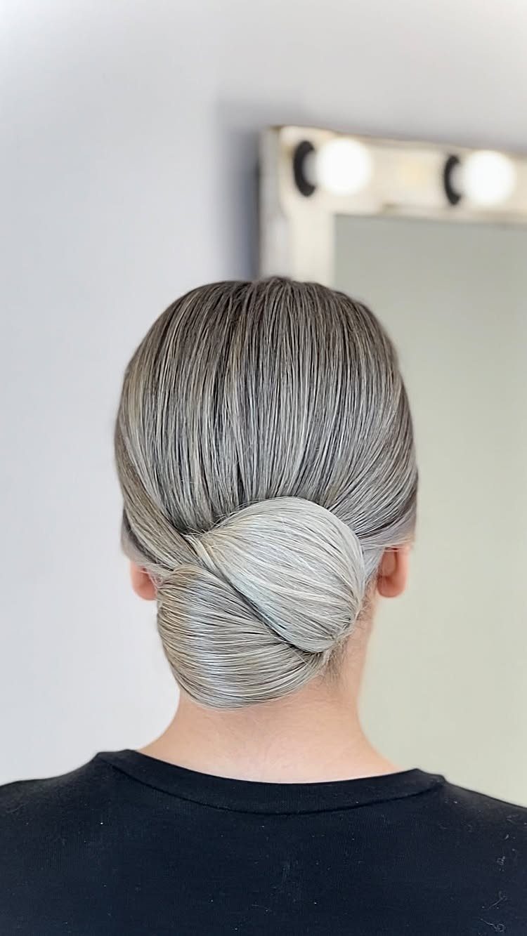 Grey hair styled into a polished, smooth chignon bun at the nape.