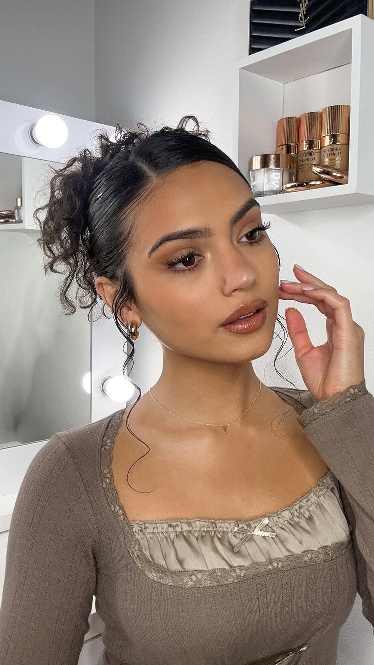Woman with a curly updo and loose tendrils wearing a brown top.