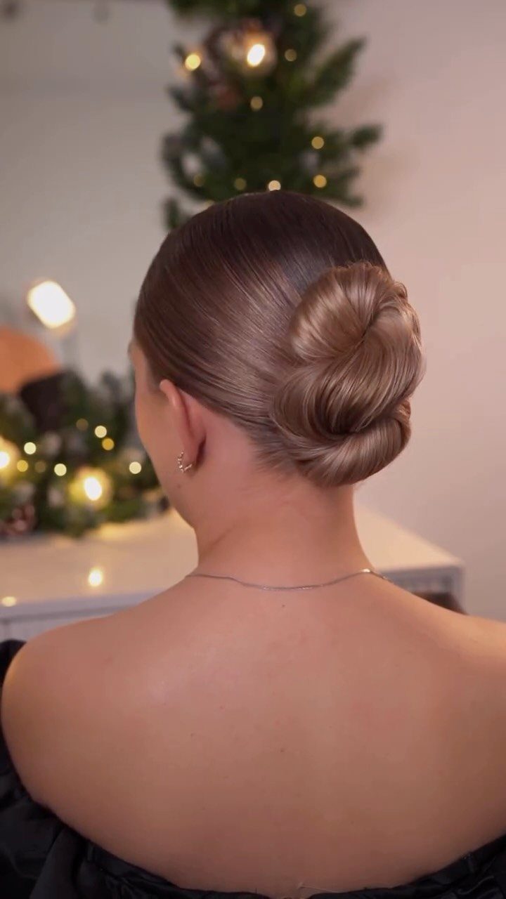 Woman with light brown hair styled in a polished low bun from behind.