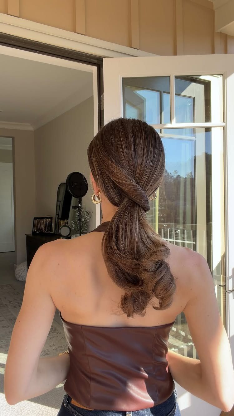 Woman with brown hair in a low twisted ponytail with curled ends.