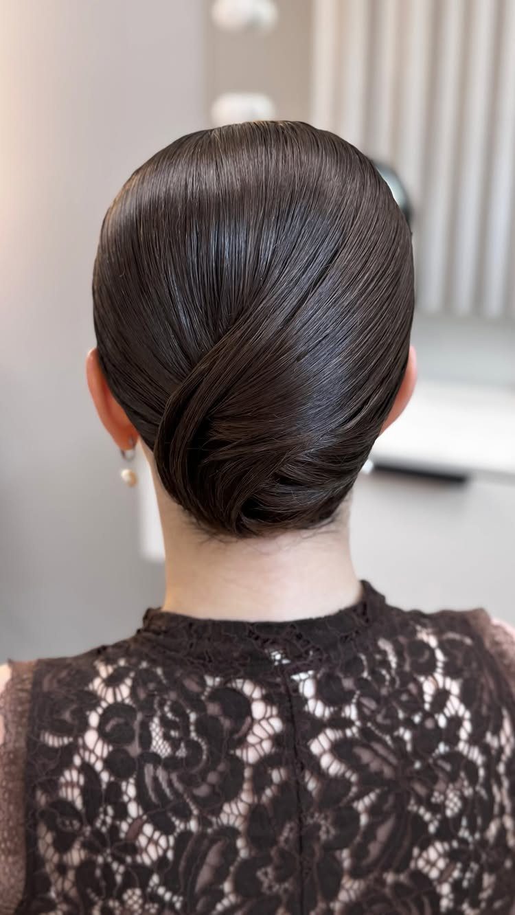 Dark brown hair styled in a sleek, glossy low bun with lace clothing.
