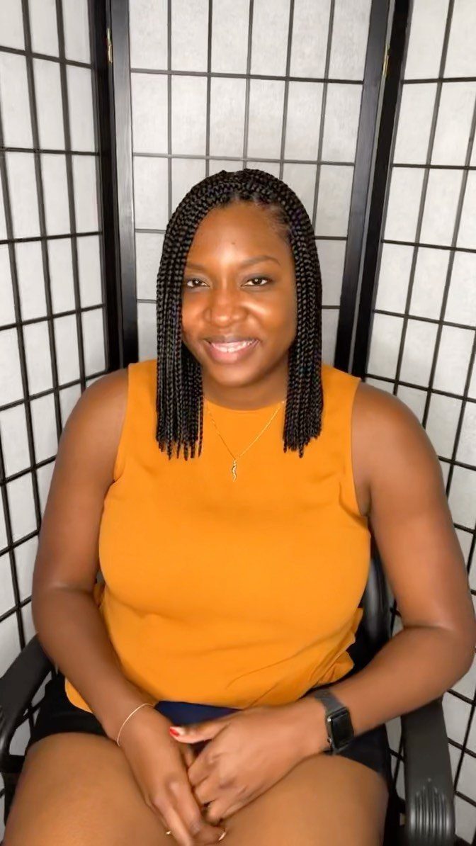 23 Hairstyles with Black Hair: Braids, Cuts, and Buns 4 Woman with shoulder-length black box braids wearing a mustard yellow sleeveless top.