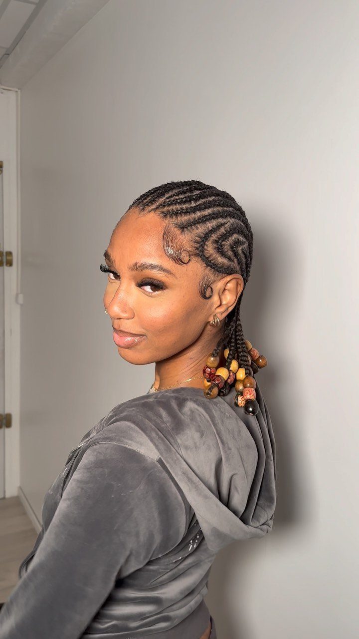 23 Hairstyles with Black Hair: Braids, Cuts, and Buns 5 Woman with black cornrow braids in a curved pattern and beaded ponytail.