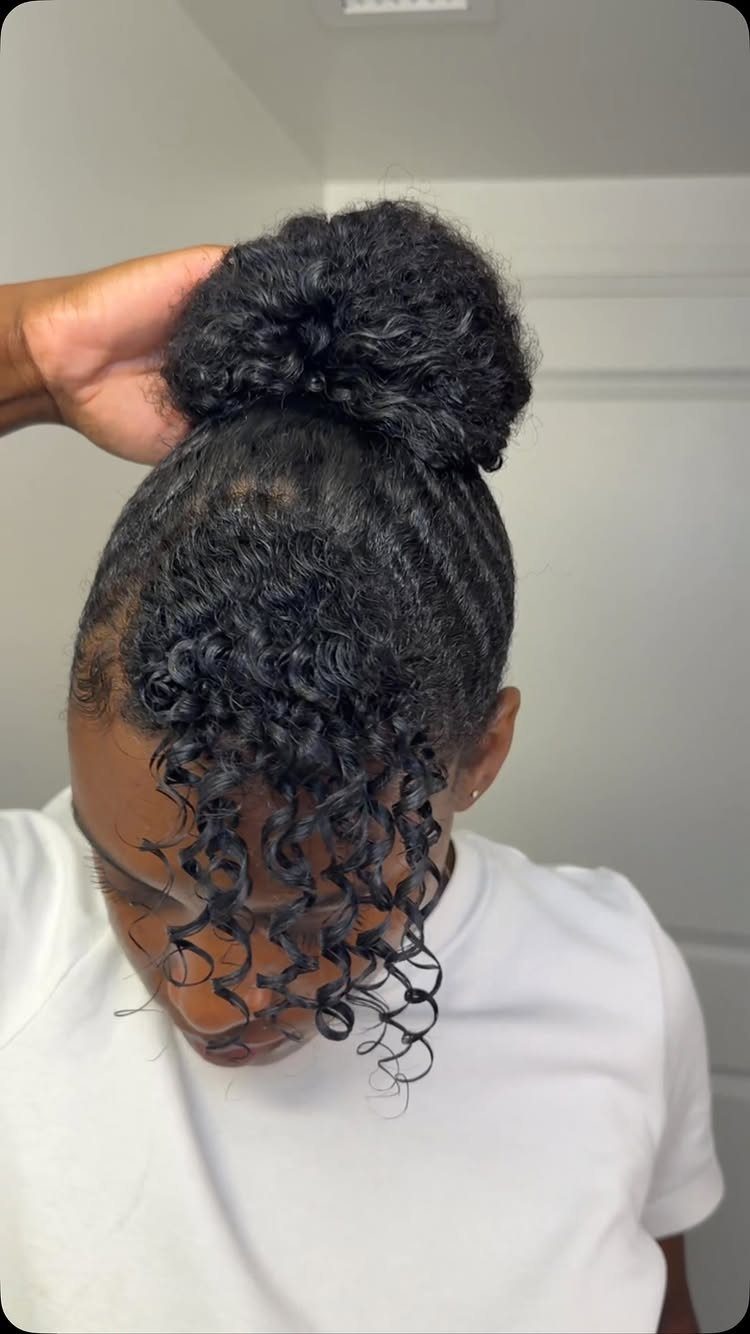 23 Hairstyles with Black Hair: Braids, Cuts, and Buns 10 Person with black hair featuring a high curly bun and curly bangs.
