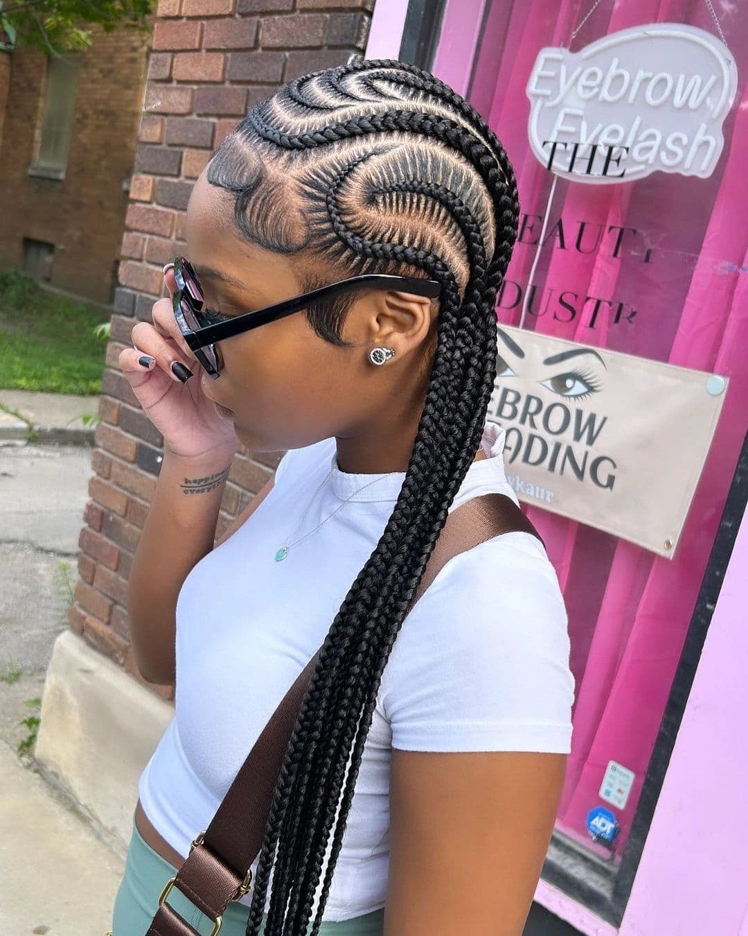 23 Hairstyles with Black Hair: Braids, Cuts, and Buns 20 Woman with black feed-in cornrow braids wearing sunglasses and a white t-shirt.