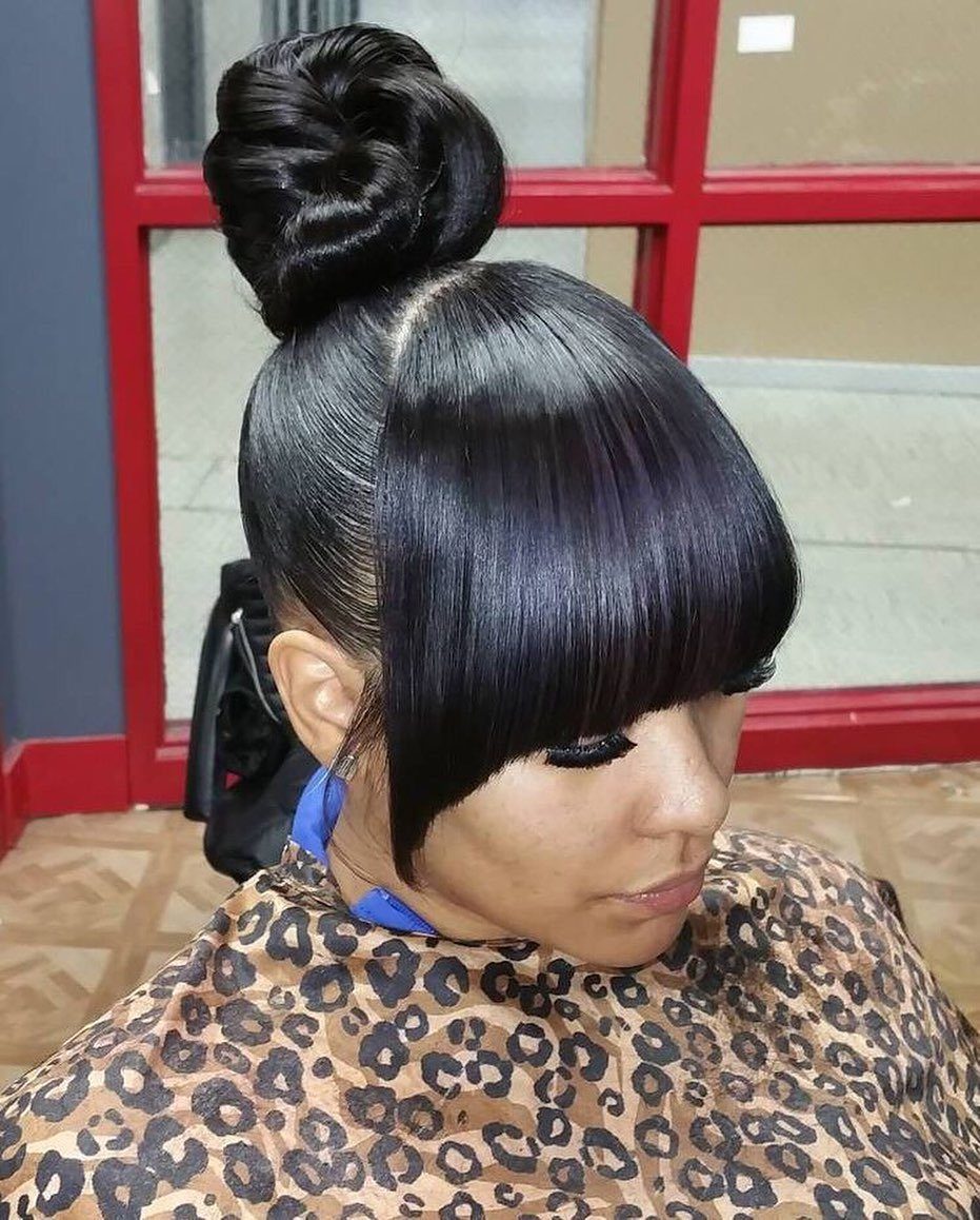 23 Hairstyles with Black Hair: Braids, Cuts, and Buns 21 Woman with sleek black hair in a high bun and blunt bangs.