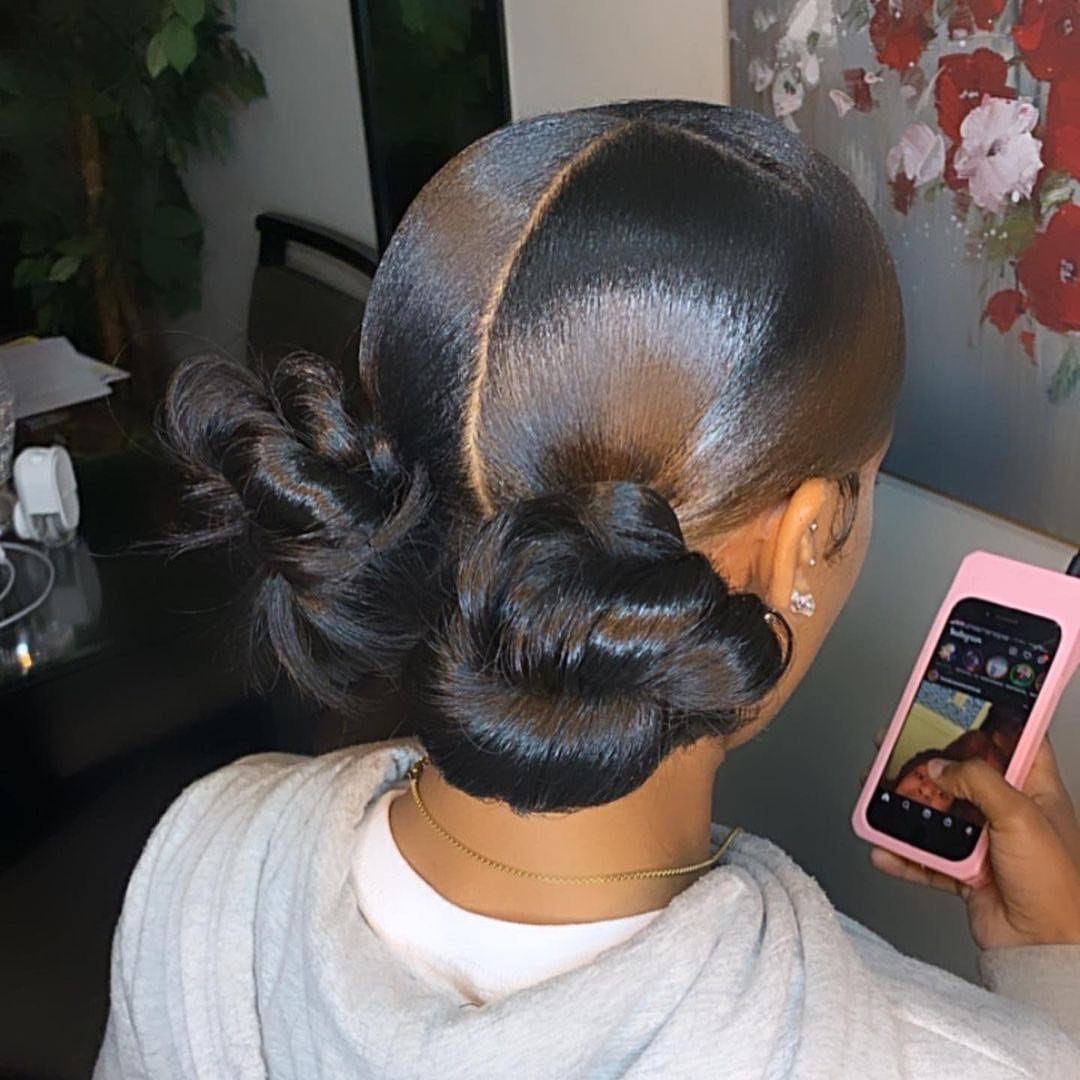23 Hairstyles with Black Hair: Braids, Cuts, and Buns 12 Woman with sleek black hair styled into two symmetrical space buns.