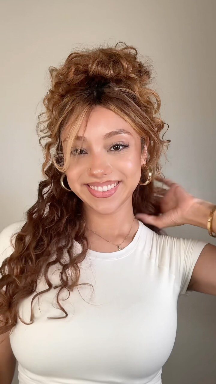 16 Homecoming Hair Curly Ideas: Buns, Braids, and Puffs 6 Woman with curly brown hair in a high half-updo and curtain bangs smiling.