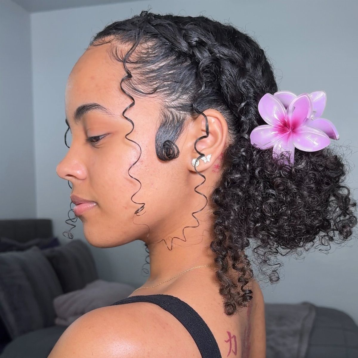 16 Homecoming Hair Curly Ideas: Buns, Braids, and Puffs 14 Woman with curly hair in a low ponytail adorned with a purple flower