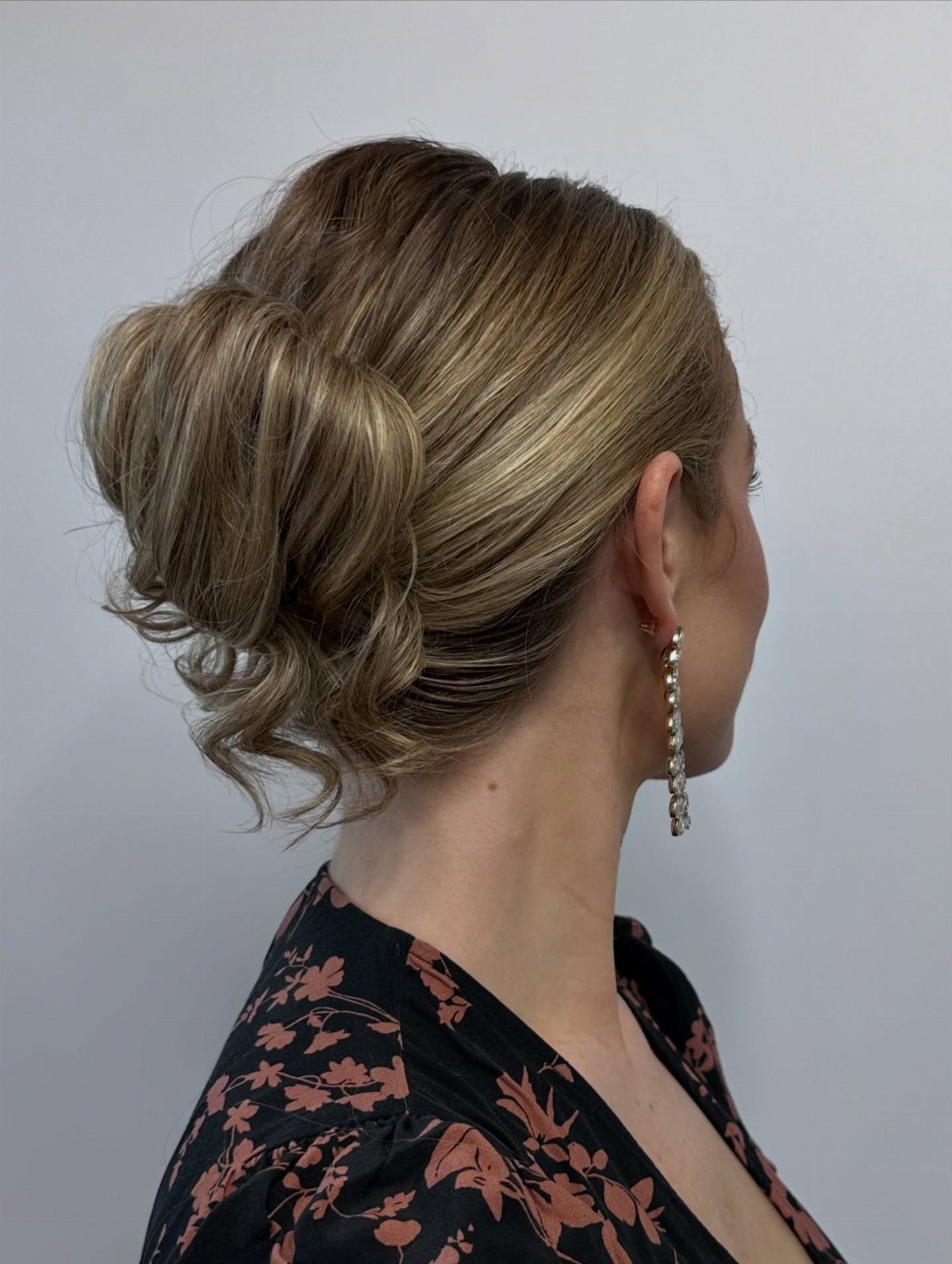 16 Homecoming Hair Curly Ideas: Buns, Braids, and Puffs 11 Woman with blonde hair in a low curly bun wearing floral dress