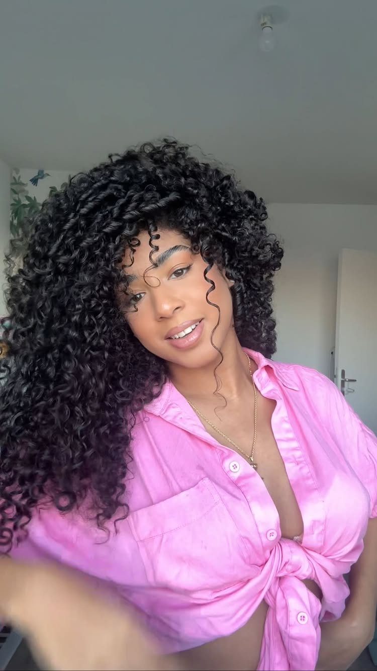 Long 3c Curly Hair Looks, Color and Updos: 15 Picks 11 Woman with long voluminous black 3c curly hair wearing a pink tied shirt.
